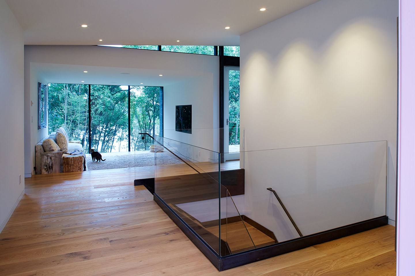 Clear glass railing at the top of the stairs in a modern home. Solid piece of glass with a base fixture.