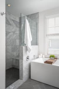 Shower and tub area that uses a glass divider as the shower door and barrier. This bathroom is styled with marble title and white bathtub.