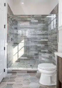 Shower and toilet area of a bathroom. This shower is using a glass door with sliding mechanics. The tile in the shower and floor use differing textures and patterns.