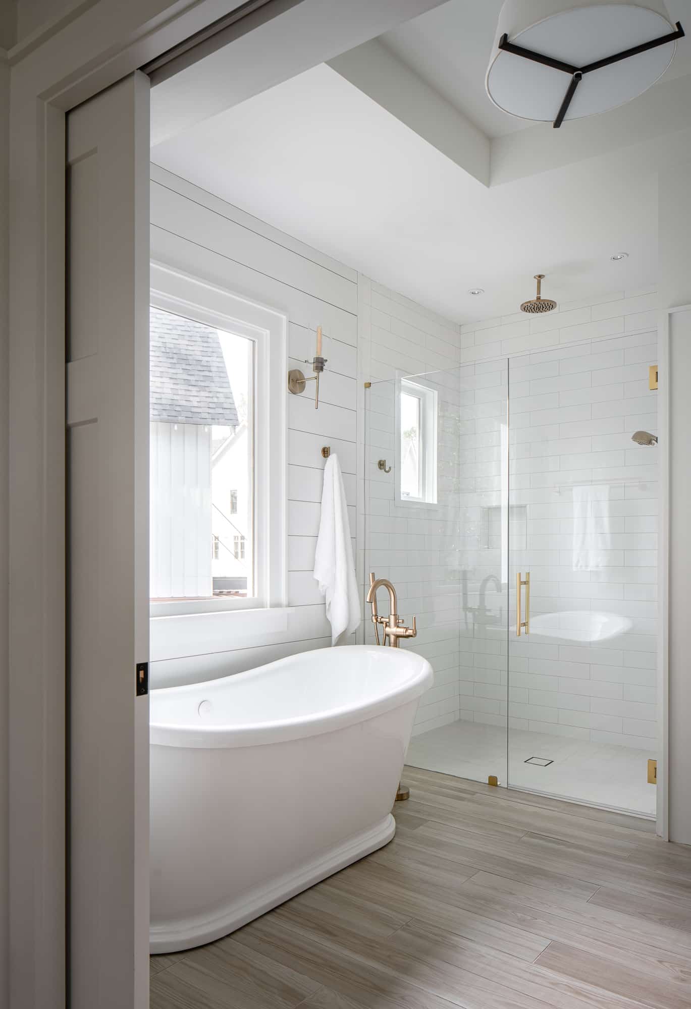An elegant bathroom with a stand-alone tub and shower with gold hardware. The shower has a traditional swinging door.
