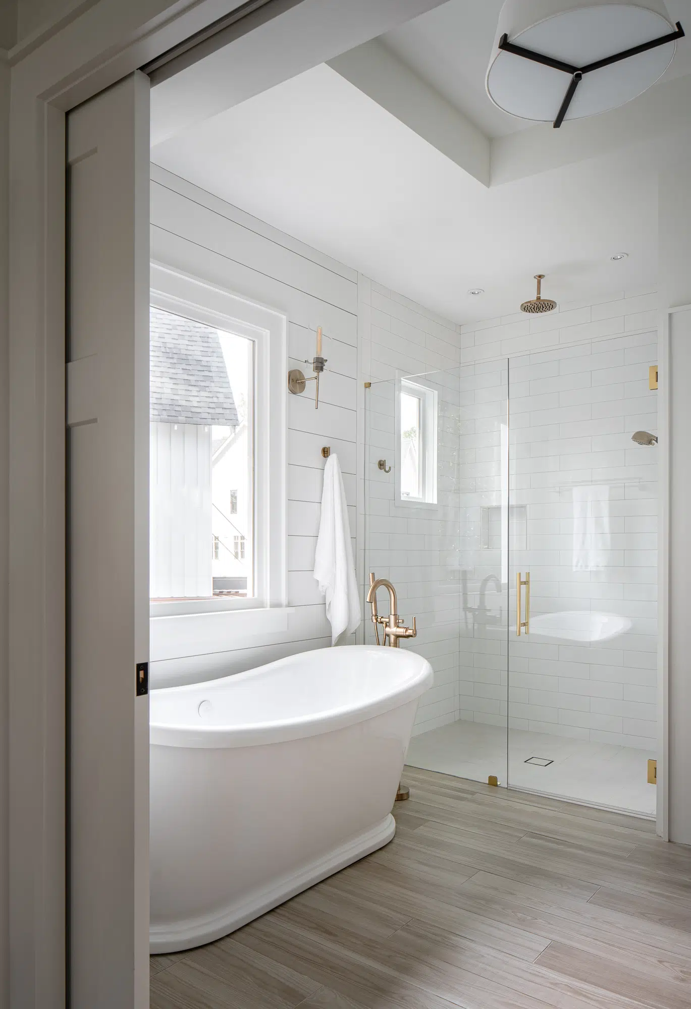 An elegant bathroom with a stand-alone tub and shower with gold hardware. The shower has a traditional swinging door.